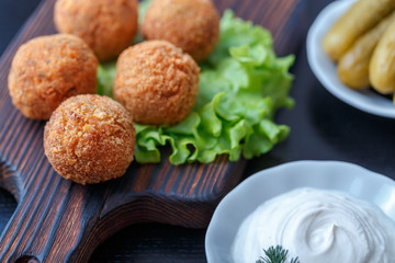 Falafel lies on a wooden cutting board. On the table lie tomatoes, cucumbers, lettuce, salad, dill, lemon, sour cream.