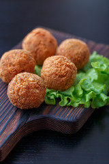 Falafel lies on a wooden cutting board. On the table lie tomatoes, cucumbers, lettuce, salad, dill, lemon, sour cream.