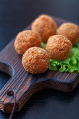 Falafel lies on a wooden cutting board. On the table lie tomatoes, cucumbers, lettuce, salad, dill, lemon, sour cream.