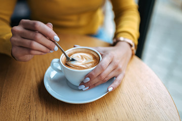 Young woman holding coffee spoon and stirring hot coffee on wooden table. Close-up.