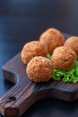 Falafel lies on a wooden cutting board. On the table lie tomatoes, cucumbers, lettuce, salad, dill, lemon, sour cream.