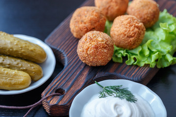 Falafel lies on a wooden cutting board. On the table lie tomatoes, cucumbers, lettuce, salad, dill, lemon, sour cream.