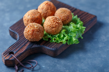 Falafel lies on a wooden cutting board. On the table lie tomatoes, cucumbers, lettuce, salad, dill, lemon, sour cream.