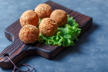 Falafel lies on a wooden cutting board. On the table lie tomatoes, cucumbers, lettuce, salad, dill, lemon, sour cream.