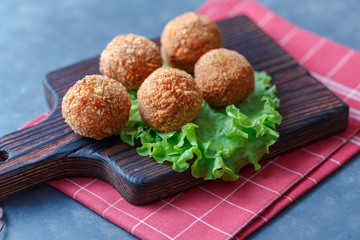 Falafel lies on a wooden cutting board. On the table lie tomatoes, cucumbers, lettuce, salad, dill, lemon, sour cream.