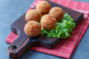 Falafel lies on a wooden cutting board. On the table lie tomatoes, cucumbers, lettuce, salad, dill,...