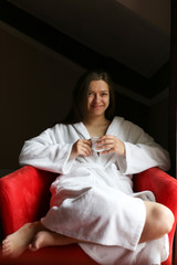 Portrait of the beautiful woman dressed in a bathrobe drinking tea in the morning in the hotel room.  	