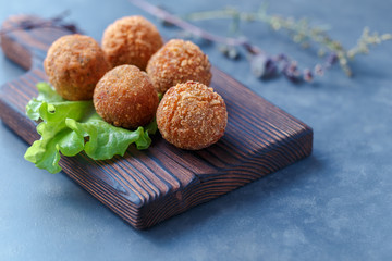 Falafel lies on a wooden cutting board. On the table lie tomatoes, cucumbers, lettuce, salad, dill, lemon, sour cream.