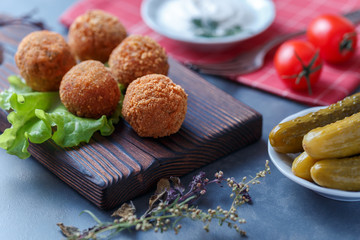Falafel lies on a wooden cutting board. On the table lie tomatoes, cucumbers, lettuce, salad, dill, lemon, sour cream.