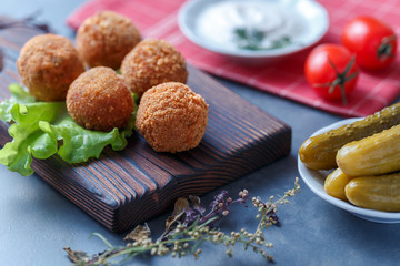 Falafel lies on a wooden cutting board. On the table lie tomatoes, cucumbers, lettuce, salad, dill, lemon, sour cream.