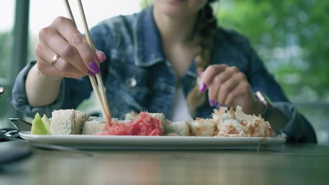 Young brunette woman takes sushi chopsticks and eats sushi. Cafe. Cose up view
