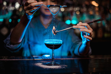 Girl adding to a brown cocktail and pour on a flamed badian on tweezers a powdered sugar in the...