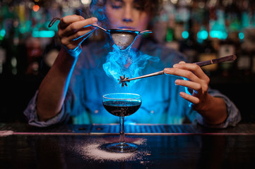 Girl adding to a brown cocktail and pour on a flamed badian on tweezers a powdered sugar through...