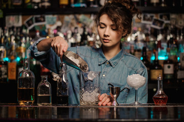 Bartender girl adding to the measuring glass cup an ice cubes