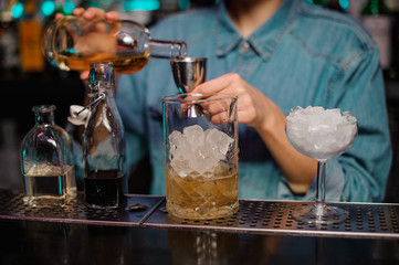 Fototapeta na wymiar Female bartender pouring to the steel jigger an alcoholic drink