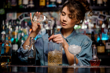 Bartender girl pouring to the steel jigger an alcoholic drink on the bar counter