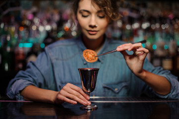Bartender girl adding a dried tomato with tweezers to a cocktail glass with alcoholic drink