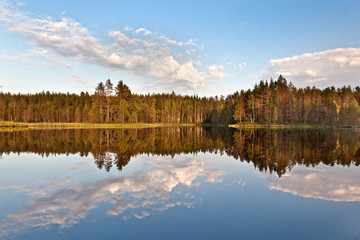 Beautiful volumetric clouds on a sunny day over a quiet forest lake