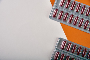 Maroon long pills, vitamins, minerals on a two-tone white and orange background. Multivitamin, drug, medicine, pill from the doctor, pharmacist. Original concept of advertising for online pharmacies.
