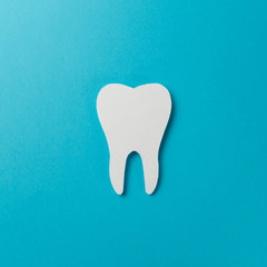 White tooth on blue background. Oral dental hygiene. Teeth whitening. Dental health concept. Oral care, teeth restoration. Dentist day concept. Flat lay. Top view. Pastel colors