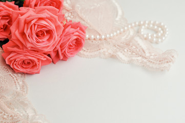 Delicate feminine theme. Pink coral roses trend color on a pale pink bra and pearl necklace on a white background. top view. close up. Stylish lingerie flat lay. Underwear fashion concept