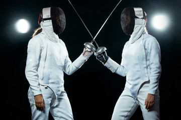 Young fencer athlete wearing mask and white fencing costume. holding the sword on black background...