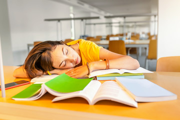 tired student girl sleeping on the stack of books in the library. Deadline and exam concept
