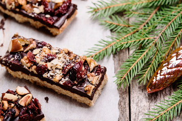 Baked shortbread sticks with chocolate, chopped nuts and dried cranberries glazed. .Millionaire's shortbread cookies and fir branches on vintage wooden table. Christmas baking