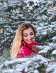 Outdoor waist up portrait. Young beautiful happy smiling girl walking on pine forest . Model with blue eyes,wearing stylish sweater. Magic snowfall. Space for text