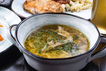 Bowl of chicken soup. Chicken soup in a white plate on a black wooden table. Free space for text. View from above. Top view.