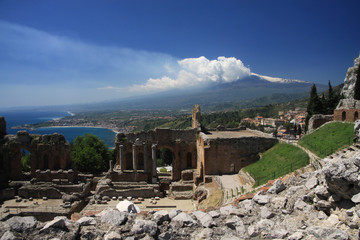 dymiący wulkan etna na sycylii z niebieskim morzem i ruinami starożytnego włoskiego miasta w tle...