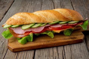 sandwich with ham, cheese, tomatoes, cucumbers, lettuce on dark wooden background