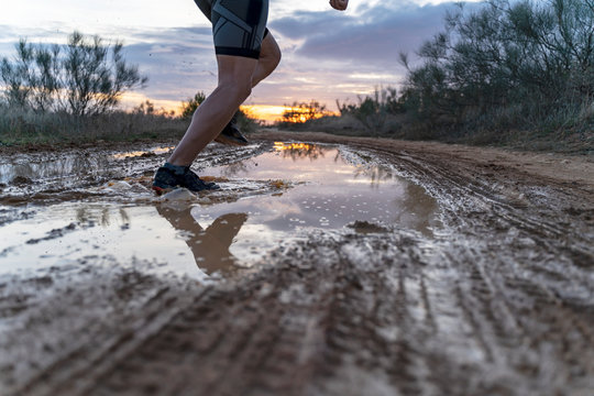 Running in the field at sunset in shorts, with sneakers, along a path with puddles that reflect the sunset.