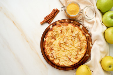 Cheesecake, apple pie, curd dessert with polenta, apples, almond flakes and cinnamon on white kitchen table, top view, copy space