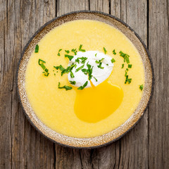 Polenta, porridge with Parmesan cheese and poached egg, on old dark wooden background, top view....