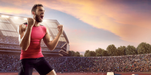 Happy male athlete. Man sprinter in sport clothes emotionally rejoices victory at the running track...