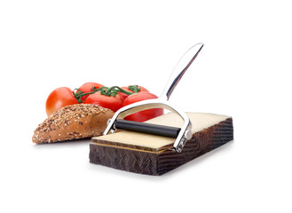 Un cortador inox de quesos en lonchas junto a un trozo de pan y unos tomates en rama sobre un fonco blanco