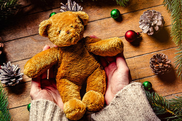 Female hands holding Christmas teddybear toy on wooden table. Personal point of view
