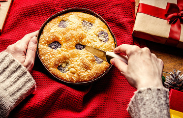 Female hands holding Christmas pie with gifts around on wooden table. Personal point of view