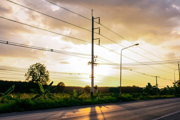 Row of electricity pole on green nature road in Thailand, Transmission line of electricity against blue sky clouds background, electricity transmission pylon with sunset light, Dawn time on road