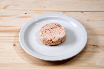 Solid white albacore tuna fish up close on white plate still shaped like the can it came in on wooden table.