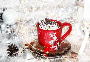 Christmas, xmas red cup of whipped cream on shiny plate, and metallic background, with chocolate, sweets, cinnamon, winter cone, lights and balls