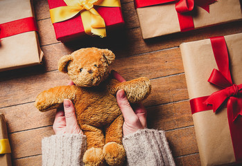 Woman hands holding teddy bear toy with gifts around on wooden table