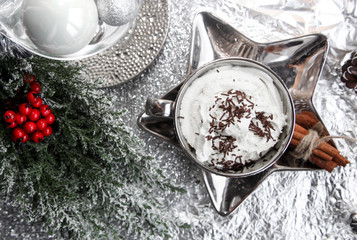 Christmas, xmas silver cup of whipped cream on shiny plate, white reindeer, red mountain ash, rowan, and metallic background, with sweets, cinnamon, winter cone, and lights