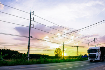 Row of electricity pole on green nature road in Thailand, Transmission line of electricity against blue sky clouds background, electricity transmission pylon with sunset light, Dawn time on road