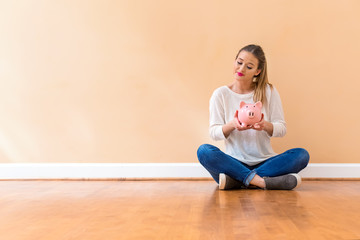 Fototapeta na wymiar Young woman with a piggy bank against a big interior wall
