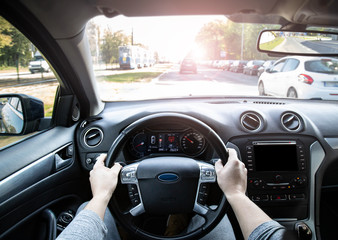 POV driver holding steering wheel in car driving through city traffic