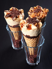 Three caramel ice cream cones, set in glasses filled with sugar crystals, on dark brown background