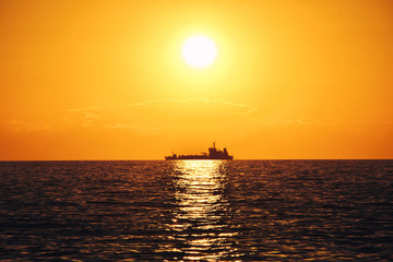 Boat crossing the horizon under the sun towards sunset.