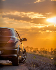 Fototapeta na wymiar beautiful black modern car stands on asphalt road in summer illuminated by the rays of the sunset